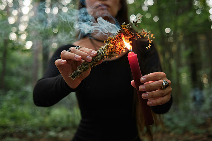 Person lighting dried herbs with a candle in forest, illustrating ridiculous cures offered to chronically ill people.
