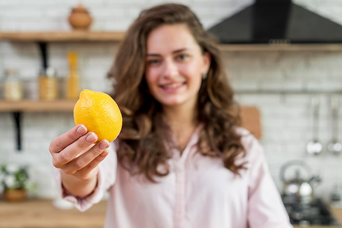 Young woman in a kitchen holding a lemon, illustrating one of the most ridiculous cures offered to chronically ill people.