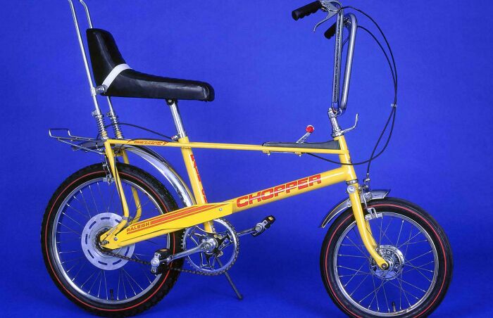 Yellow vintage toy bicycle with high back seat and Chopper logo, a collectible vintage toy worth fortune against blue background