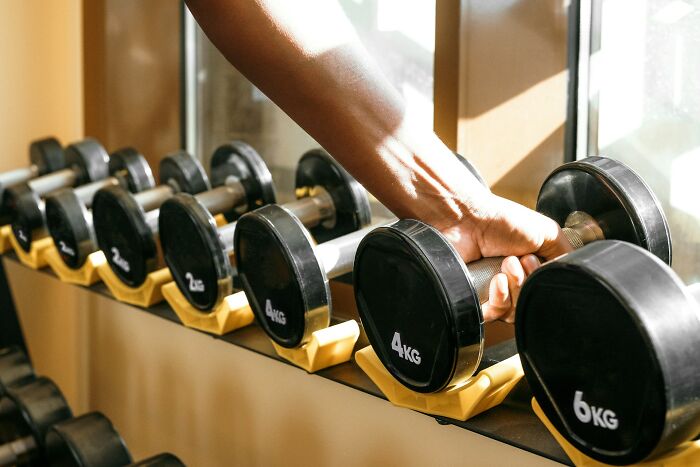 Person using a loophole by adjusting dumbbells in a gym with weights ranging from 2 to 6 kilograms.
