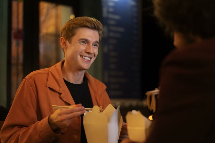 Young man smiling on a date while using chopsticks, illustrating common red flags in women’s dating tests.