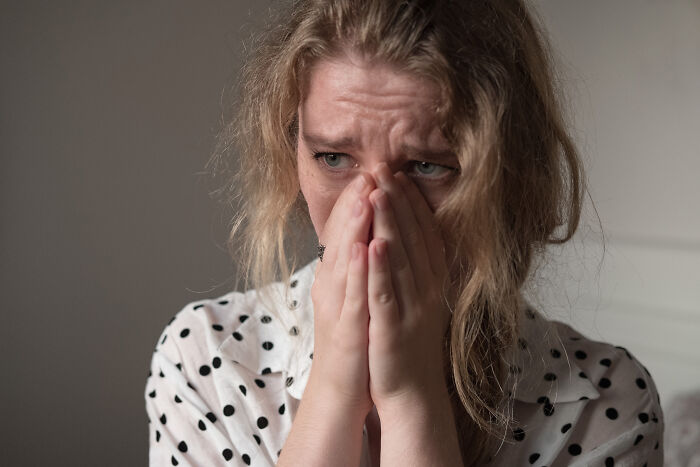 Stressed woman in polka dot shirt covering face, representing doctors and nurses sharing haunting experiences.