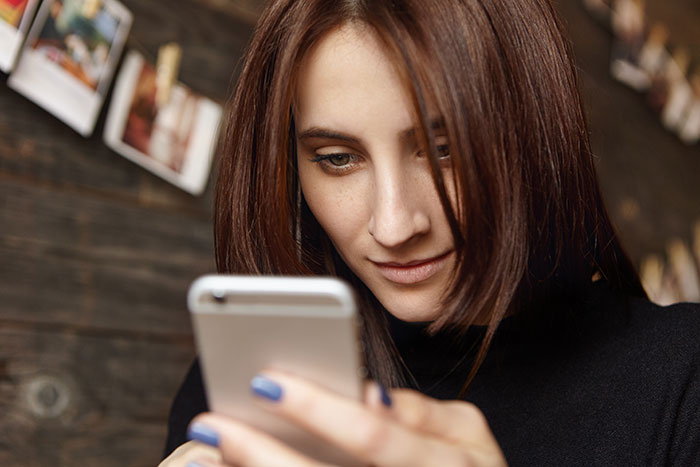 Young woman with brown hair staring intently at her smartphone, concerned about family drama aired online by a half-sister. Young woman with brown hair staring intently at her smartphone, concerned about family drama aired online by a half-sister.