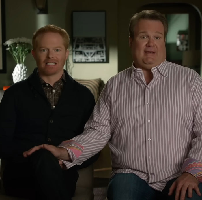 Eric Stonestreet and Jesse Tyler Ferguson sitting together in a living room scene from Modern Family.