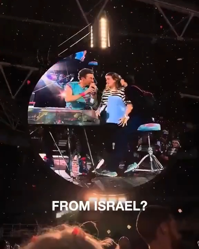 Chris Martin on stage interacting with fans during a concert, amid political speech backlash and controversy.