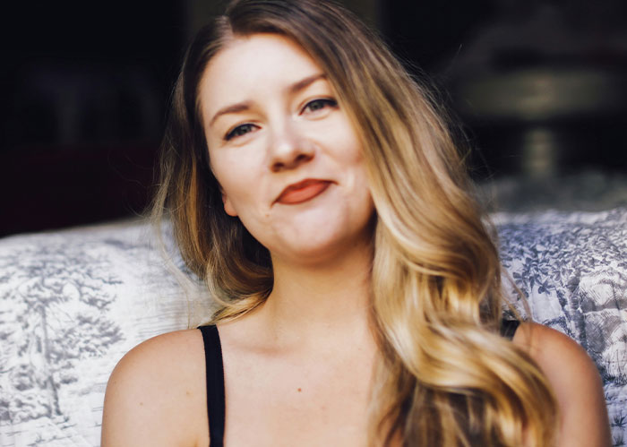 Young woman with long blonde hair smiling slightly while sitting indoors, representing student petty revenge after loud music at 2 a.m.