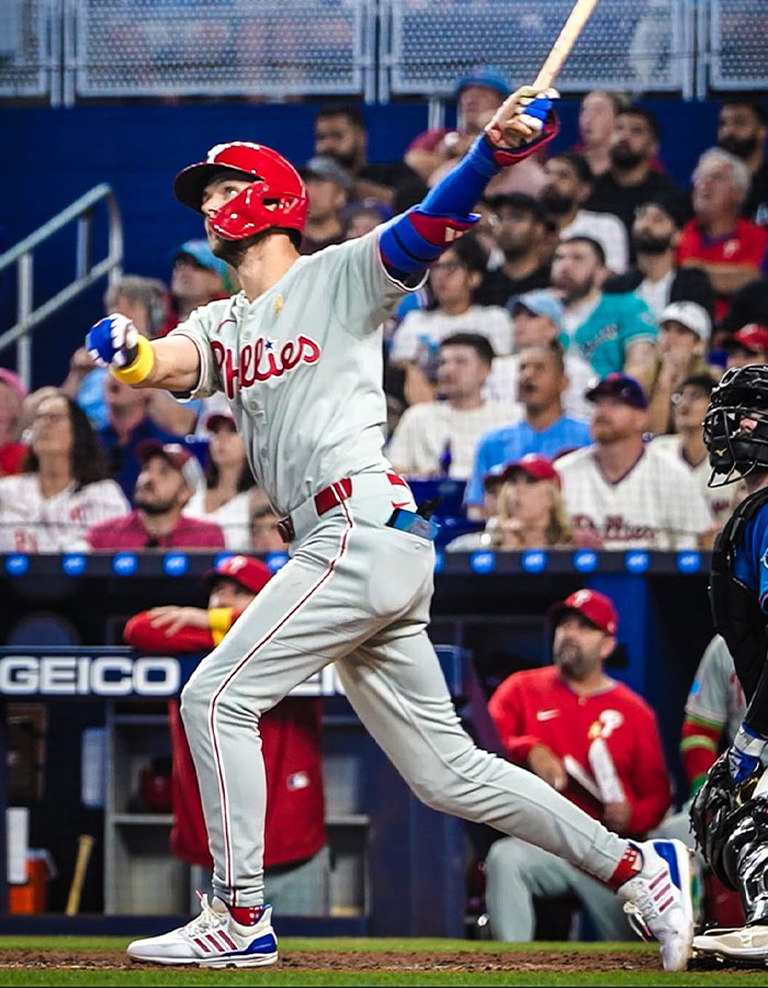 Baseball player in Phillies uniform swinging bat during game with crowd watching, related to Karen snatching home run ball.