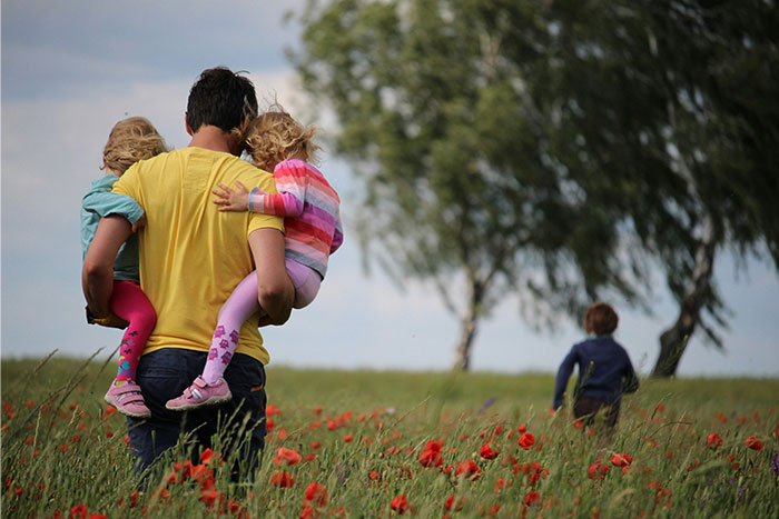 Man carrying two young girls in a field of red flowers while a boy walks ahead, illustrating family and abandoned son themes. Man carrying two young girls in a field of red flowers while a boy walks ahead, illustrating family and abandoned son themes.