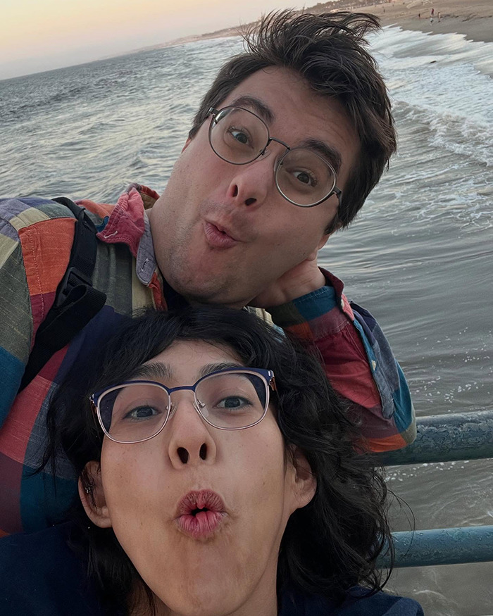 Couple by the ocean sharing a playful moment, representing conjoined twin and husband discussing intimacy in their marriage.