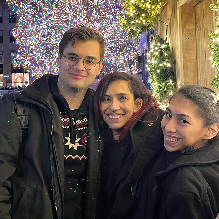 Young couple and conjoined twin smiling outdoors near festive holiday lights, sharing a moment despite intrusive questions about intimacy.