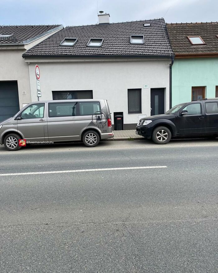 Two cars parked in front of a small house with a narrow black door and windows in a bizarre construction design.
