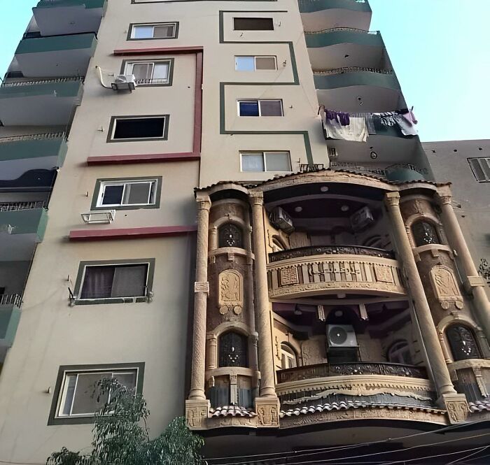 Unconventional building design featuring mismatched windows and an ornate balcony that looks like a construction fail.