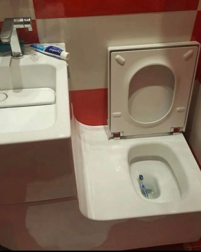 Toothbrush placed inside a toilet bowl next to a sink in a poorly designed construction and design setup.