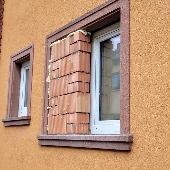 Window partially blocked with bricks and foam on an orange exterior wall, showcasing unconventional construction design flaws.