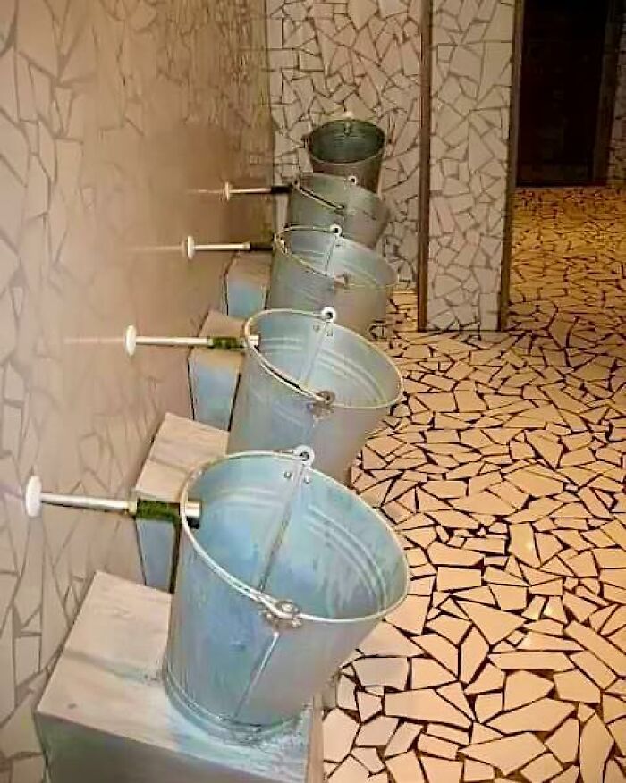 Buckets mounted on wall as urinals in a bathroom with mosaic tile floors and walls, a strange construction design example.