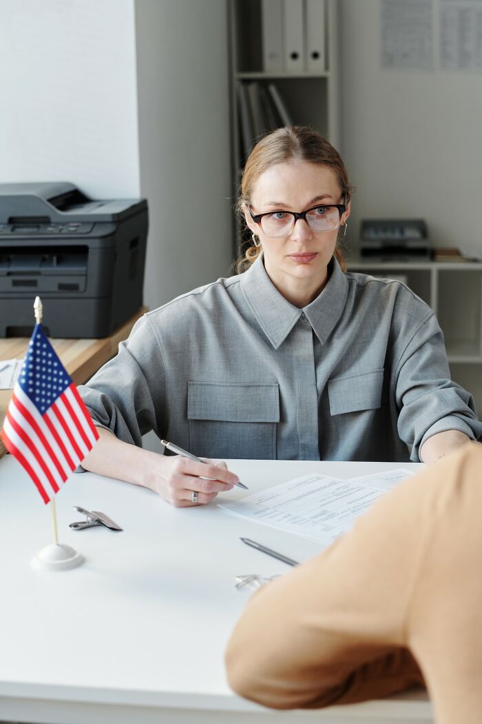 Woman in glasses reviewing documents at a desk with an American flag, illustrating Americans finding a loophole.
