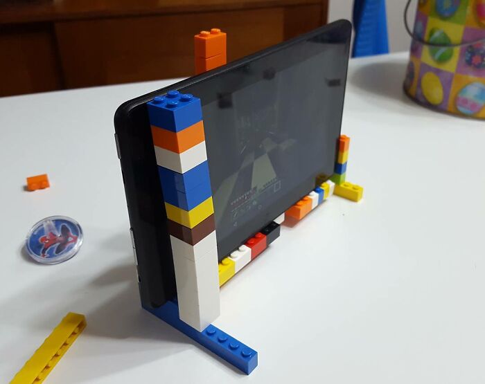 Kids' creative invention of a colorful Lego phone stand holding a tablet on a white table surface.