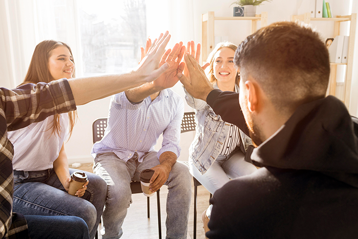 Group of friends giving a high five indoors, representing a schizophrenic man prank hospital visit concept in casual setting.