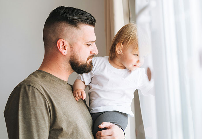 Man holding toddler by window, highlighting family concern and impact of essential oils poisoning incident.