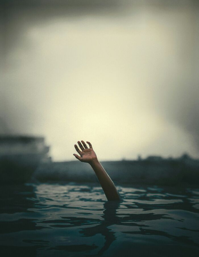 A single hand reaching out of dark water symbolizing escaping death by pure luck in a dramatic and moody setting.