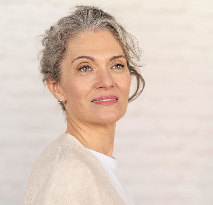 Mature woman with gray hair looking thoughtful, representing crazy things heard from MILs needing to calm down.