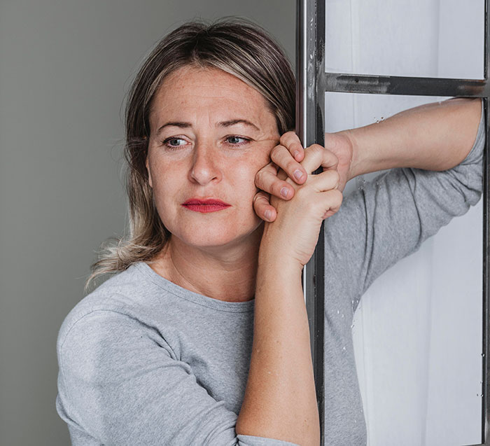 Woman in gray shirt looking thoughtfully out window, reflecting on crazy things heard from MILs that really need to calm down.
