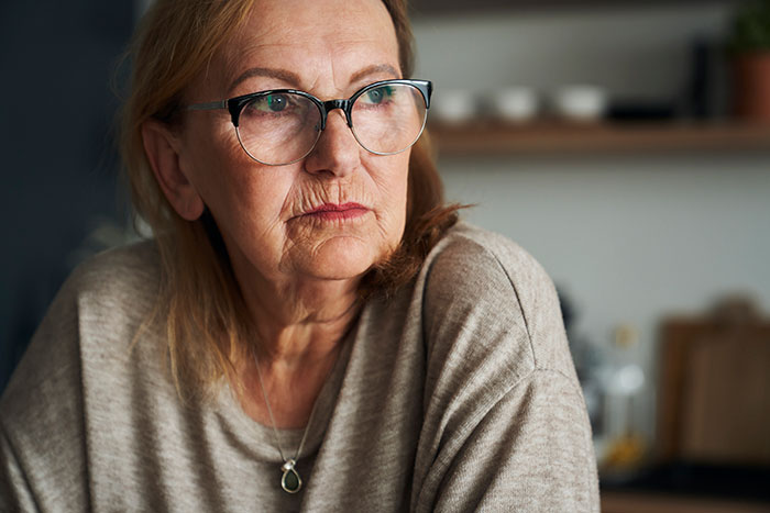 Older woman with glasses looking thoughtful indoors, illustrating crazy things heard from MILs needing to calm down moments.