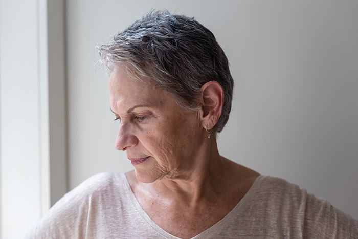 Older woman with short gray hair looking down pensively near natural light, illustrating crazy things heard from MILs.