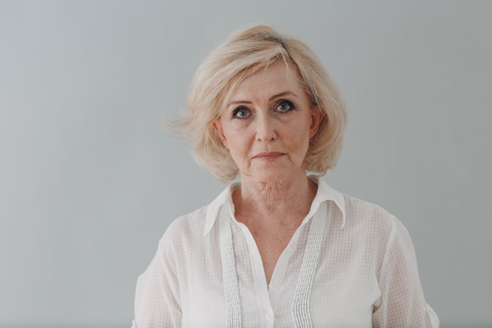 Serious older woman with blonde hair in a white blouse representing crazy things heard from MILs needing to calm down