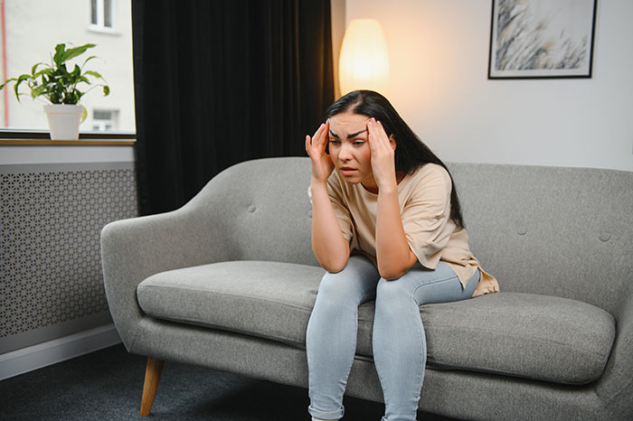 Woman sitting on a couch with a stressed expression, illustrating crazy things heard from MILs causing frustration.