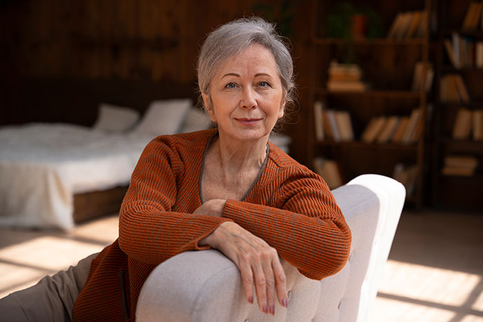 Older woman in rust sweater sitting on a chair looking calm, illustrating crazy things heard from MILs needing to calm down.