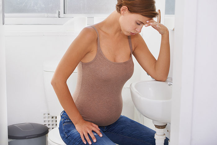 Pregnant woman sitting on a toilet, looking distressed, representing crazy things heard from MILs that really need to calm down.