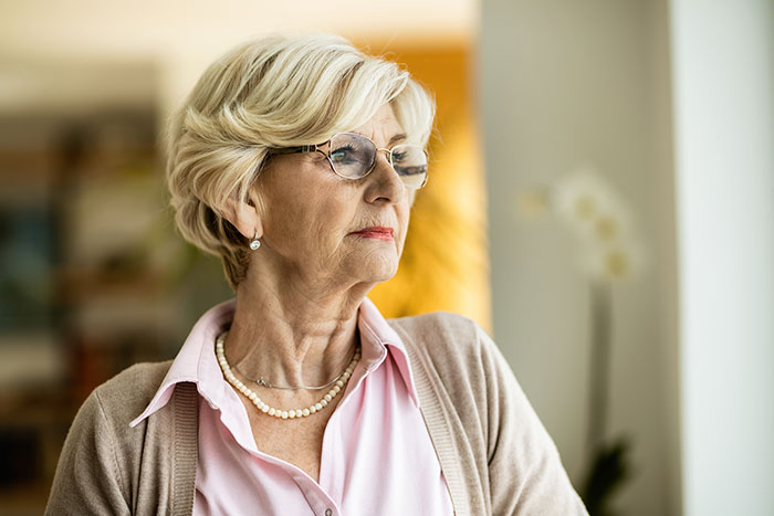 Elderly woman with short blonde hair and glasses looking out window reflecting on crazy things heard from MILs.