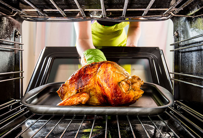 Person wearing green oven mitts placing a roasted chicken in the oven, illustrating crazy things heard from MILs.