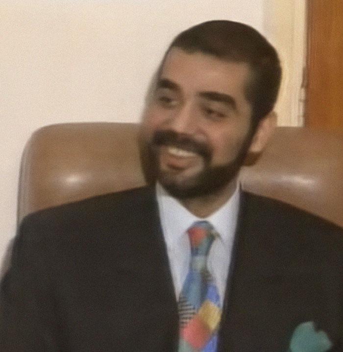 Man in suit sitting on a chair, smiling and showing interest, representing history anecdotes about the past.