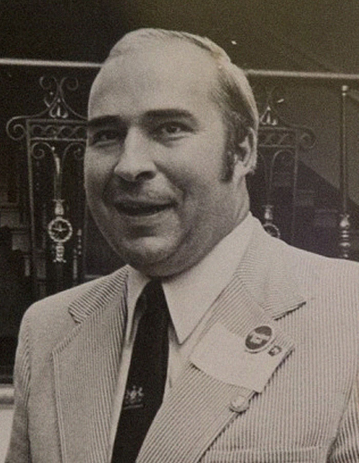 Black and white portrait of a smiling man in a suit, representing history anecdotes about the past.