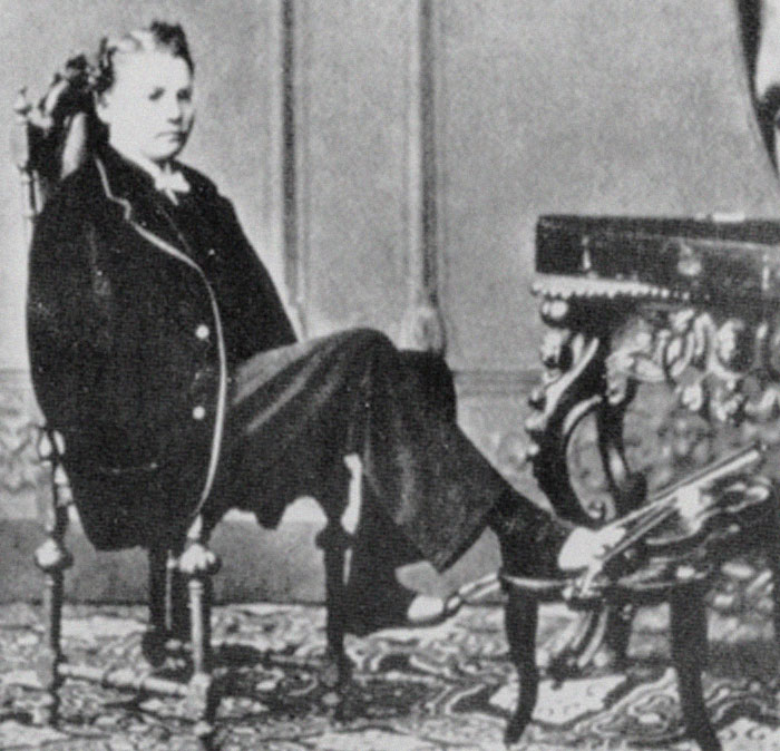 Black and white photo of a man in Victorian attire sitting with feet on an ornate table, illustrating history anecdotes.