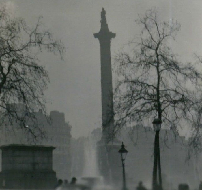 Black and white photo of a tall historic monument surrounded by bare trees and foggy cityscape, history anecdotes theme.