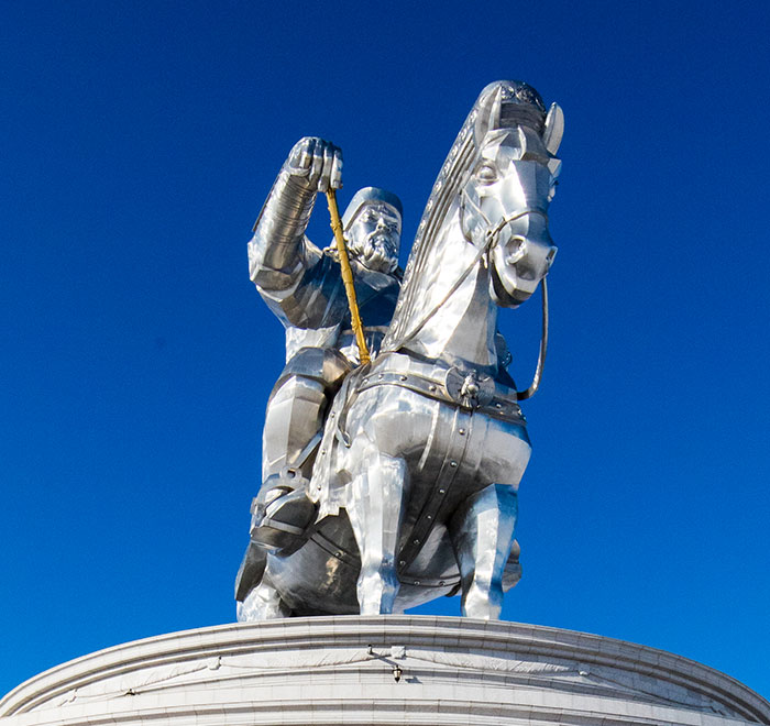 Shiny metal statue of a medieval knight on horseback under clear blue sky, reflecting history anecdotes and the past.