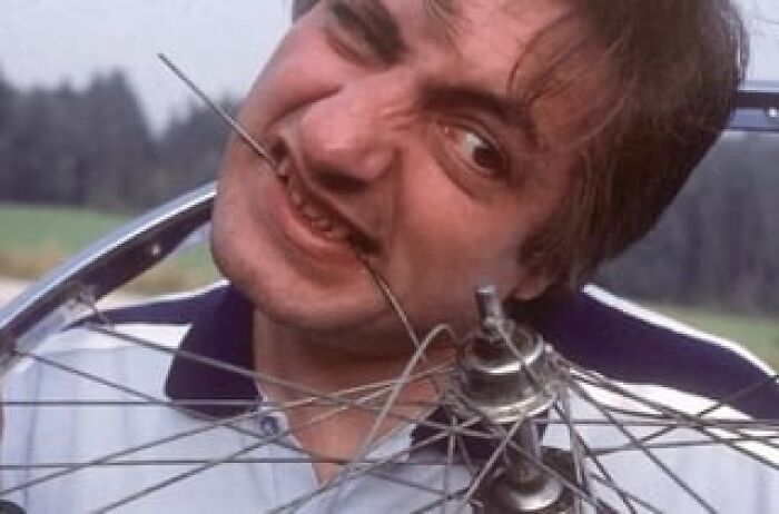 Man biting bicycle wheel spokes outdoors, illustrating unusual history anecdotes that teach something new about the past.