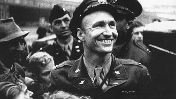 Smiling World War II soldier surrounded by people, capturing a moment from history anecdotes about the past.