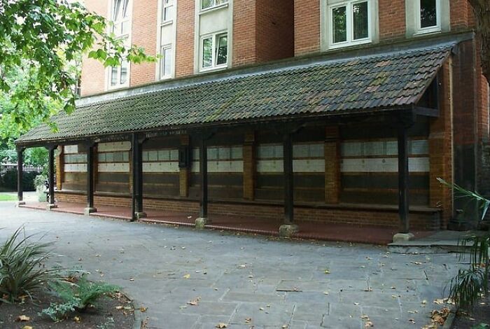 Old brick building with covered walkway, surrounded by greenery, reflecting history anecdotes and past architectural styles.