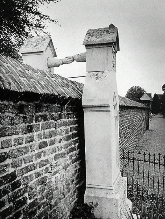 Black and white image of two stone chimneys with sculpted hands shaking above a brick wall, a unique historical anecdote.
