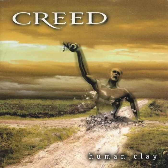 Creed Human Clay album cover with a distorted figure rising from a c*****d dirt road, known as a bad album cover.
