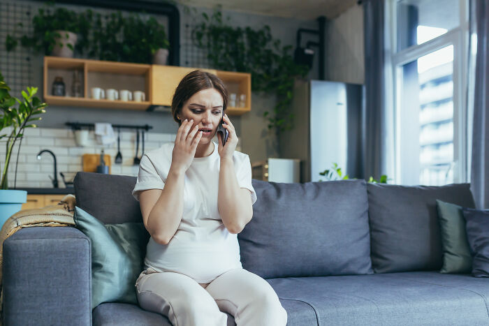 Woman looking distressed while receiving a bizarre phone call at home, reacting as if wanting to throw her phone out the window.