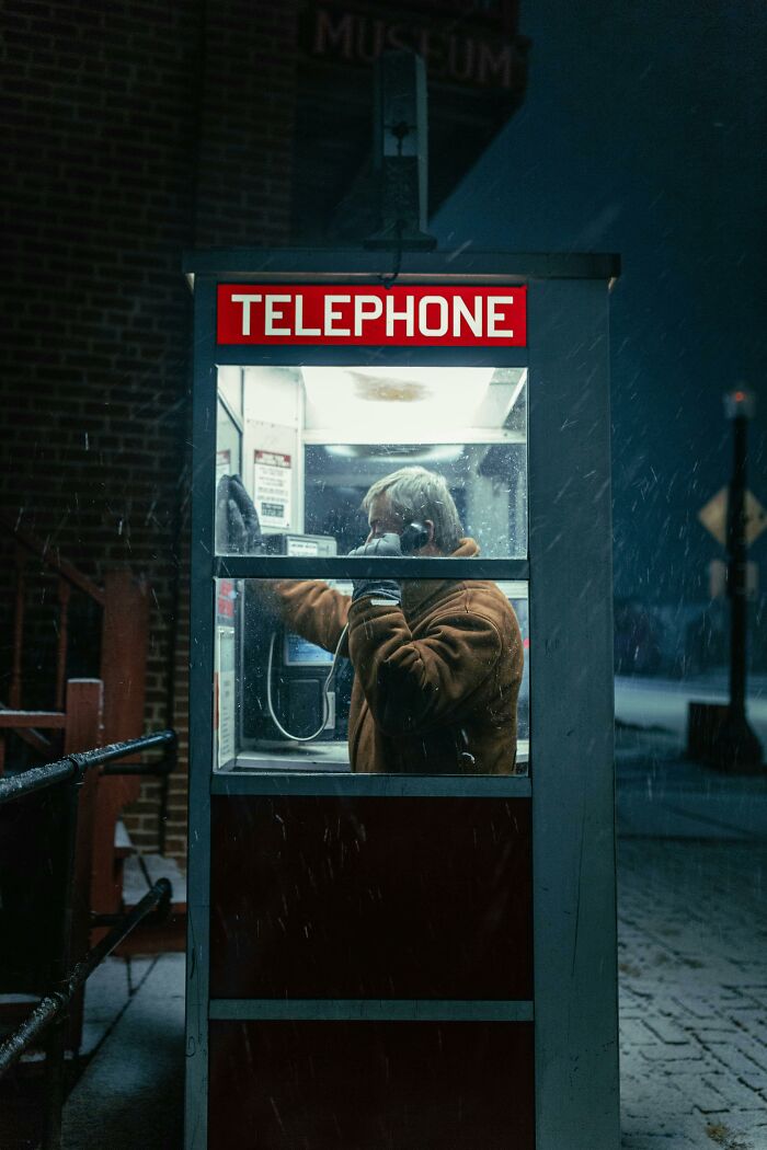 Person in a telephone booth making a phone call at night, illustrating bizarre messages and phone calls concept.