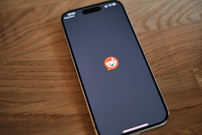 Smartphone displaying Reddit app icon on a wooden surface representing bizarre messages and phone calls.