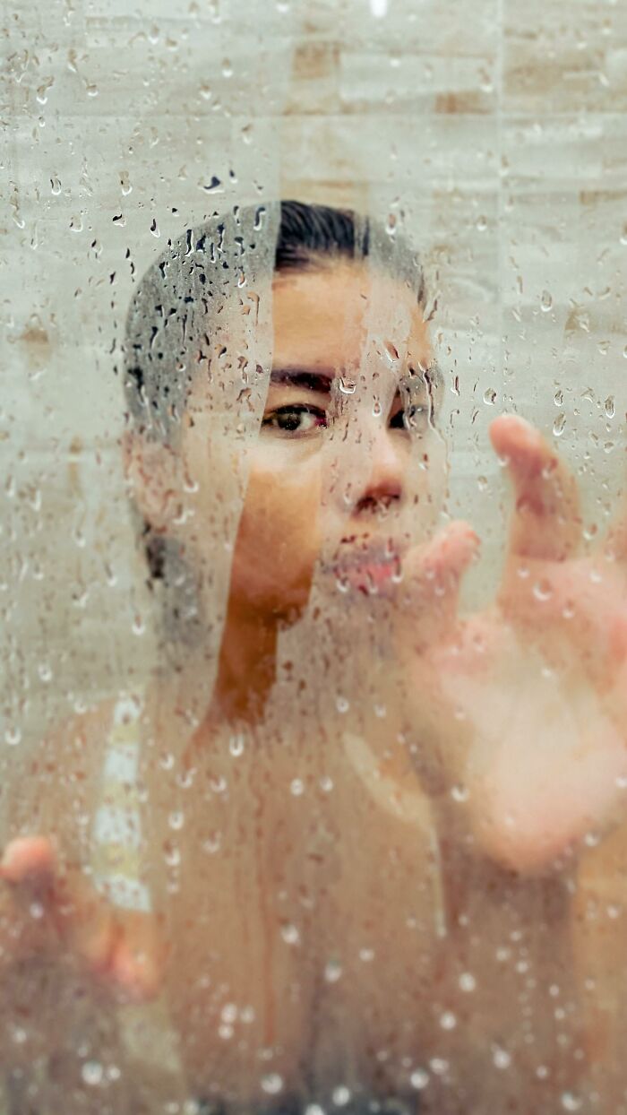 Person behind a wet glass pane, touching the surface, illustrating feelings from bizarre messages and phone calls.