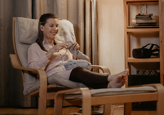 Woman knitting in a cozy chair at home, relaxed and smiling, where people can’t explain these creepy things experienced.
