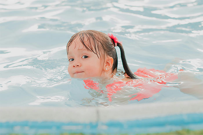 Young girl swimming in a pool with wet hair, reflecting on creepy things people can’t explain they’ve experienced.